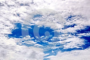 White clouds of various shapes against the blue sky and the sun above the surface of the ocean.