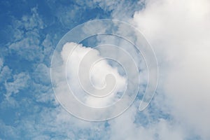 White clouds of various shapes against the blue sky and the sun above the surface of the ocean.