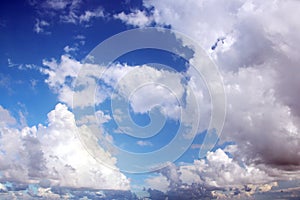 White clouds of various shapes against the blue sky and the sun above the surface of the ocean.