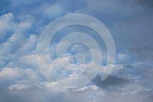 White clouds of various shapes against the blue sky and the sun above the surface of the ocean.