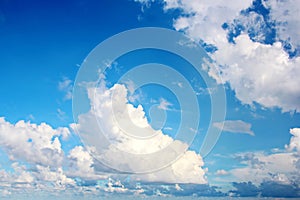 White clouds of various shapes against the blue sky and the sun above the surface of the ocean.