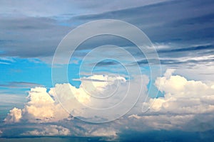 White clouds of various shapes against the blue sky and the sun above the surface of the ocean.