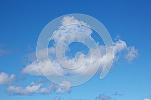 White clouds of various shapes against the blue sky and the sun above the surface of the ocean.