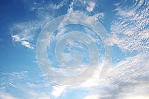 White clouds of various shapes against the blue sky and the sun above the surface of the ocean.