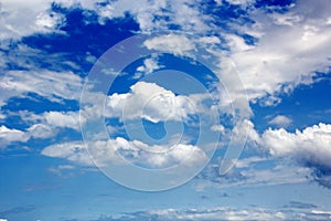 White clouds of various shapes against the blue sky and the sun above the surface of the ocean.