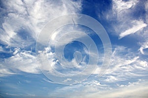 White clouds of various shapes against the blue sky and the sun above the surface of the ocean.