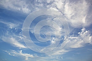 White clouds of various shapes against the blue sky and the sun above the surface of the ocean.