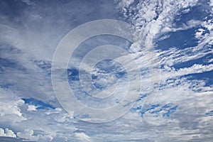 White clouds of various shapes against the blue sky and the sun above the surface of the ocean.