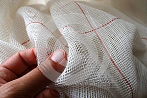 White coarse cotton or linen curtains made of weaves of thin threads. A woman& x27;s hand is feeling the fabric. Window