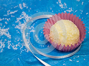 White coconut chocolate truffle in a pink candy wrapper on a blue crumpled paper background.