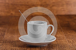 White coffe Cup with spoon on white saucer on dark brown wooden background