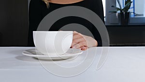 White coffee cup being put on cafe tabe in front of female guest. Coffee drinking in cosy restaurant. waiter in black