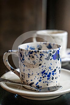 White coffee cup with blue spots on a saucer with a spoon on a wooden table