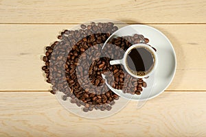 White coffee cup and coffee beans are on a wooden background.