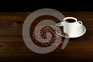 White coffee cup and coffee beans are on a wooden background.
