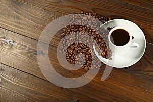 White coffee cup and coffee beans are on a wooden background.