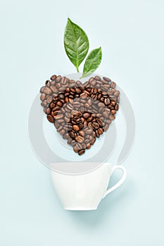 White coffee cup and coffee leaves and beans in shape of heart on blue background, flat lay