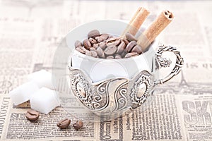 White coffee cup filled with coffee beans on newspaper with cinnamon