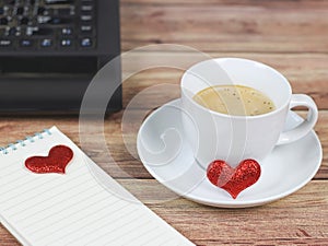 White coffee cup , notebook with red glitter hearts and computer notebook on wooden table , Valentine`s day concept