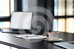 A white coffee cup is putting on contemporary workspace with empty screen computer laptop.