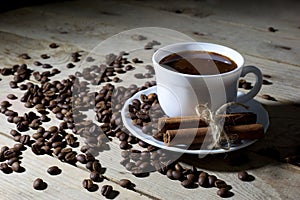 White Coffee Cup and Saucer with Cinnamon and Coffee Beans on Wooden Table