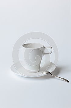 White coffee cup on a saucer and the metallic teaspoon isolated on white background