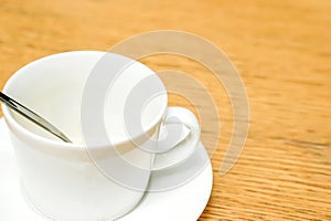 White coffee cup and spoon with saucer on wooden table