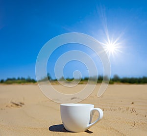 White coffee cup stay on sand under a sparkle sun