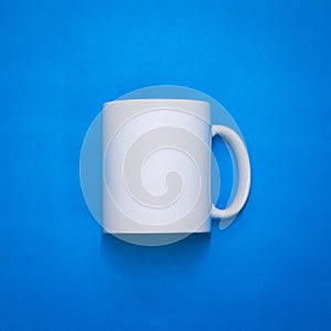 White coffee mug on blue paper background. Template of drink cup for your design. Can put text, image, and logo. Front or side