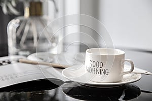 White coffee mug with bouquet of flowers lily of the valley and notes `good morning` on black modern marble table