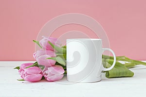 White coffee mug with pink tulips on a pink background. Space for text or design.