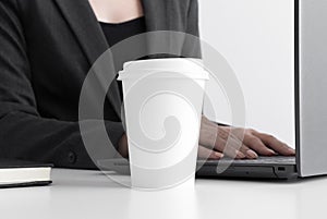 White coffee paper cup mockup with woman working on a computer