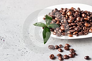 White coffee plate with roasted coffee beans on grey stone background.