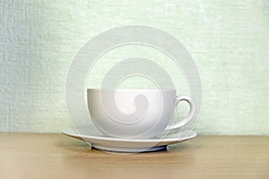 White coffee or tea cup with a saucer on a wooden table against the wall