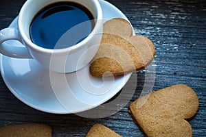 White coffeecup with hot fresh beverage and heart-shaped gingerbread biscuits. Coffee break with love. Side of coffee