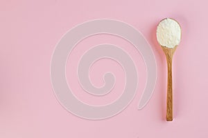 White collagen powder on a wooden spoon on a pink background. Skin care, rejuvenation. Copy space.