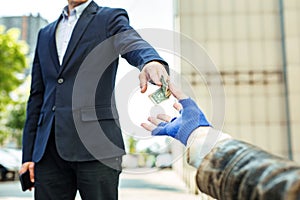 White collar worker giving dollar bill to homeless vagrant