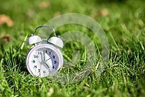 White color alarm clock on green grass. Place for text. Time, circadian rhythm, early rise concept