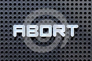 White alphabet with word abort on black pegboard background photo