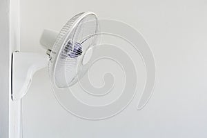 White color electric wall fan hanging on white cement wall, copy space