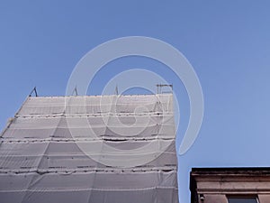 White color net covers scaffolding in town for safety and legal rules regulation, blue sky background. Building repair in a street
