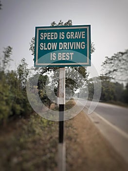 White color `speed is grave slow driving is best` text on blue color rectangular board at the highway