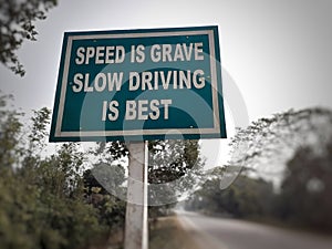 White color `speed is grave slow driving is best` text on blue color rectangular board at the highway