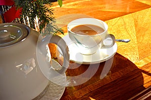 White color of Teapot and a cup of hot tea on wooden table and bright light from sun. Traditional english tea in afternoon.