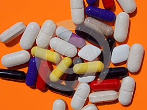 White and colored capsules on an orange background close up. Dietary and sports supplements