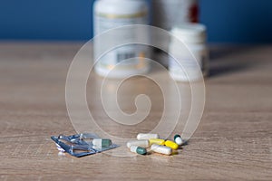 white and colored pills lie on a wooden table against the background of jars with medicines health day.