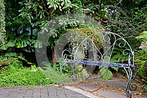 White colored wrought iron bench in the garden with tropical plants