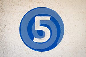White coloured hand painted level number five in the middle of a blue colour circle painted on old textured concrete pillar wall