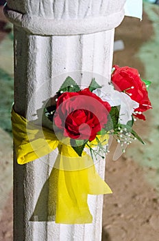 White column with two artificial red roses and yellow ribbon