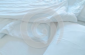 White comfort bed and soft pillow in modern bedroom. White linen blanket in hotel bedroom. Closeup detail of messy white blanket